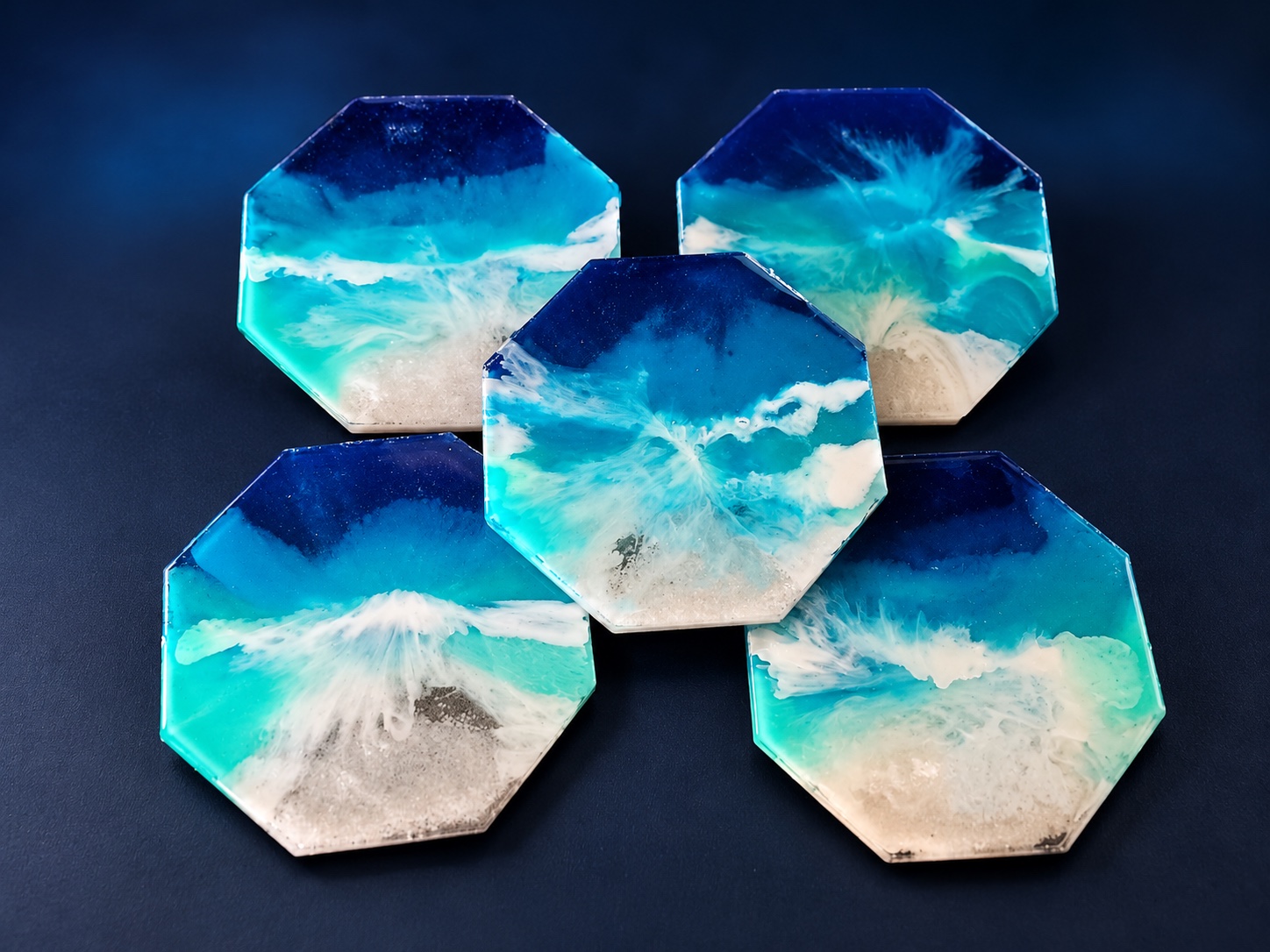 Five octagonal turquoise, cobalt, white, and sand-colored ocean resin coasters